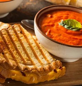 A bowl of cream of tomato soup with a grilled cheese next to it